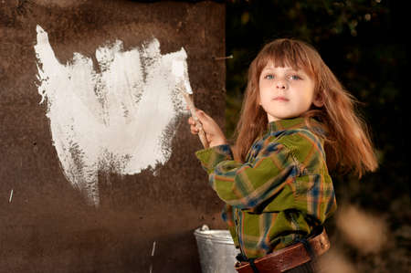 Little cute caucasian girl colouring a wall of an old destructed houseの写真素材