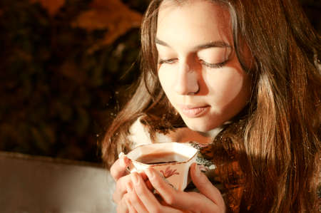 Girl sitting on the banch in a night park and taking a tea cup.