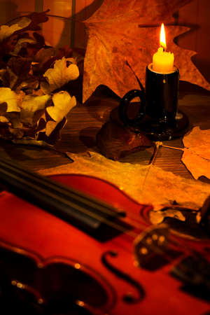 Violin and autumn leaves on the on the table in light of candle in the dark room. Focus on the candleの写真素材