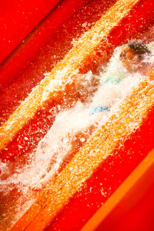 Little caucasian girl inside water splash on waterslide of water park. Summer