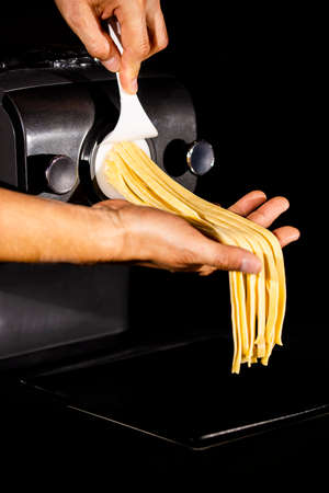 Home made pasta by pasta maker. An indifinited man cutting the tagliatelle. Selected focusの写真素材