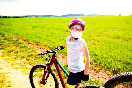 Sport and quarantine. 9 years biker girl in a mask amidst of the fields in the sunny dayの写真素材