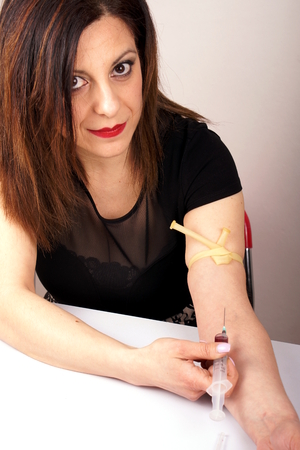 Studio shot of a lady with syringe and tourniquetの写真素材