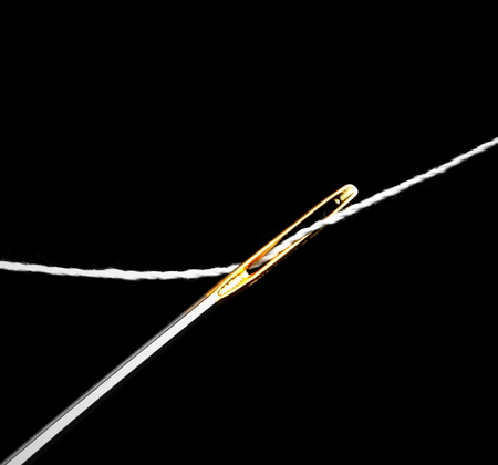Close up of a needle eye with white thread