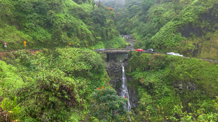 traffic slows at a narrow bridge above a waterfall on mauiの写真素材