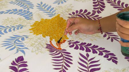 GIANYAR, INDONESIA - JUNE, 19, 2017: close up of a worker applying paint to cloth at a batik factory...