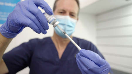 wide shot of a male healthcare worker filling a syringe with a covid-19 vaccine