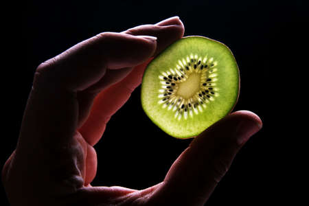 Hand holding kiwi fruit on blackの写真素材