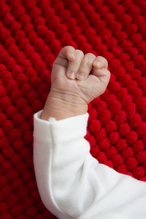 Newborn baby closed hand on red fluffy backgroundの写真素材
