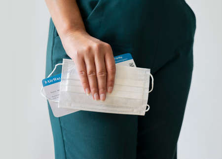 Woman standing, holding plane ticket and disposable facemask