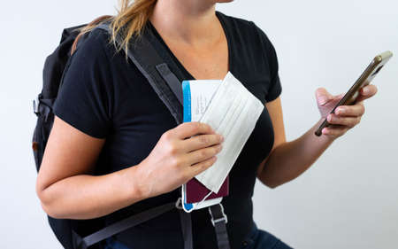 woman travelling during pandemic crisis with backpack looking on her phone, holding boarding pass,...