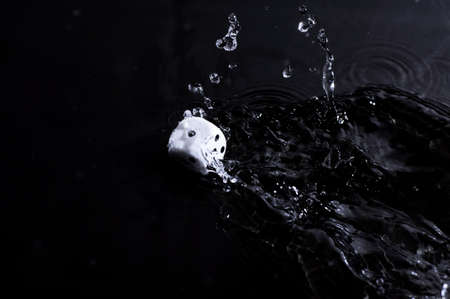 A white dice rolling into a puddle of water の写真素材