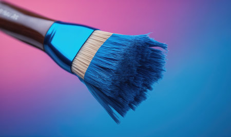 A blue paintbrush with a wooden handle rests against a gradient background of pink and blueの素材