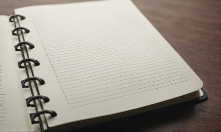 A blank page in a spiral bound notebook sits open on a wooden desk, ready for new ideas and notesの素材