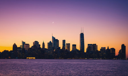 The Chicago skyline is silhouetted against a beautiful sunset, with the moon visible in the skyの素材