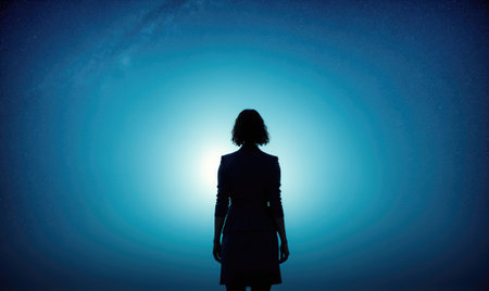A woman stands in silhouette against a bright blue skyの素材