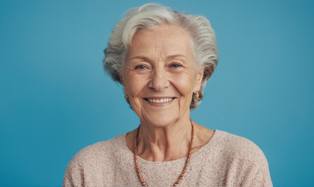 A smiling older woman with gray hair poses for a portrait against a blue backgroundの素材