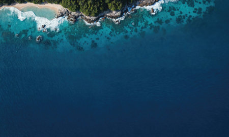 An aerial view of a sandy beach, lined with rocks and trees, meeting the clear turquoise waterの素材