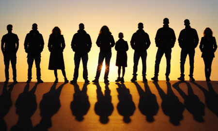 A group of people stand in a line, silhouetted against the setting sun, their shadows stretching long across the groundの素材