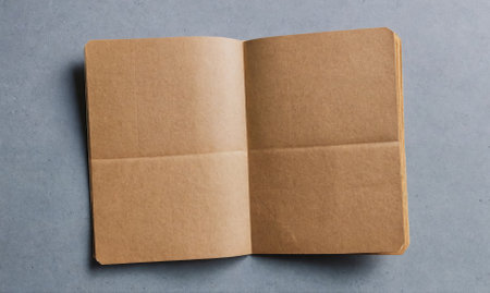 A brown notebook is open on a grey surface, ready for writingの素材