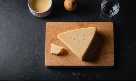 A wedge of cheese sits on a wooden cutting board, ready to be enjoyedの素材