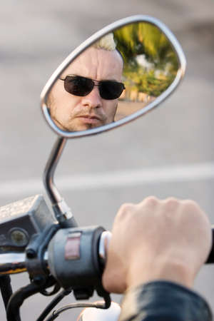 Man with a punk haircut seen in the rearview mirror of his motorcycle.の写真素材