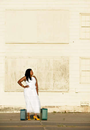 African American woman with suitcases waits outside an industrial building.の写真素材