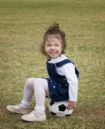 Little girl on a playground sitting on a soccer ball and making a funny face.の写真素材