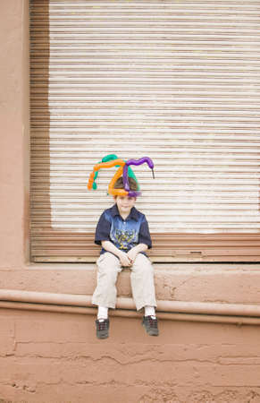 Young boy wearing a balloon hat sitting on a ledgeの写真素材