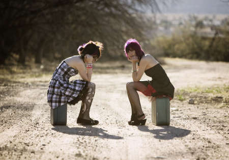 Two punk women sitting on suitcases and waiting on a rural road