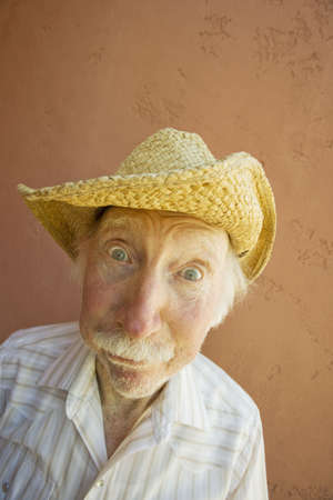 Senior Citizen Man with a Funny Expression Wearing a Straw Cowboy Hatの写真素材