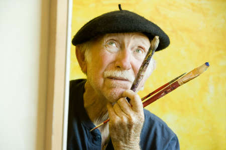 Elderly painter wearing a beret working on a large canvas and looking upの写真素材