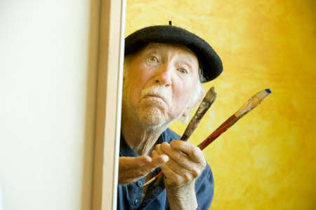Elderly painter wearing a beret working on a large canvas and looking upの写真素材