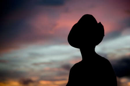 Woman in a cowboy hat silhouetted against a colorful sunset sky.の写真素材