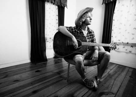 Young musician with an old guitar in an empty roomの写真素材