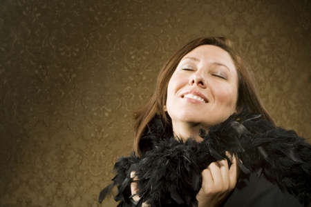 Pretty Hispanic Woman Wearing a Feather Boa in front of Gold Wallpaper