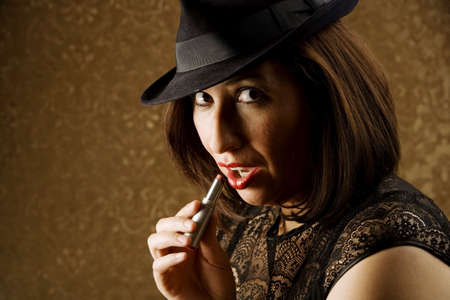 Pretty Hispanic Woman in a Fedora Applying Lipstickの写真素材