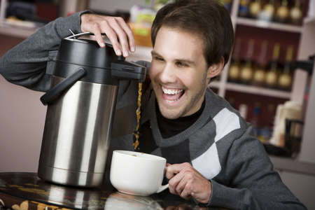 Young man crazily pouring coffee from a thermos in a cafeの写真素材