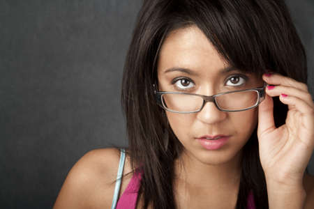 Close up portrait of a pretty brunette woman looking over her glassesの写真素材