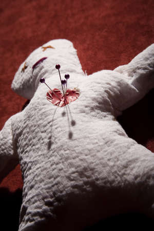 White Voodoo Doll with Pins in its Heart on Red Backgroundの写真素材