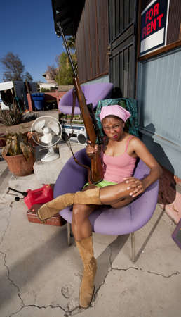 Black woman with rifle in front of house with messy yardの写真素材