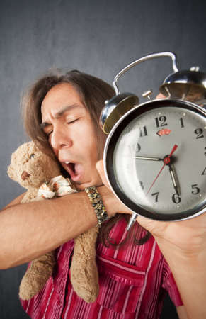 Sleepy handsome young man with long hair and alarm clockの写真素材