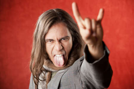 Closeup Portrait of Handsome Young Man with Long Hair Making Hand gesture and Sticking Out Tongueの写真素材