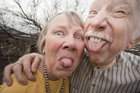 Closeup portrait of crazy elderly couple outdoors sticking out tonguesの写真素材