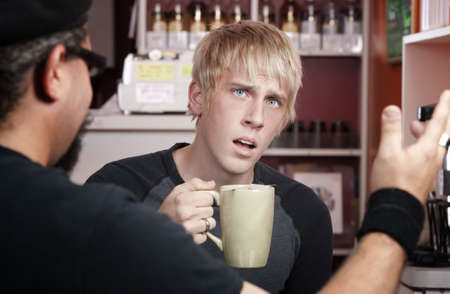 Shocked young blonde man reacting to coffee house conversationの写真素材