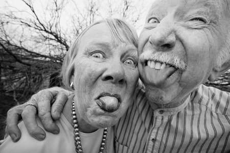 Closeup portrait of crazy elderly couple outdoors sticking out tongues