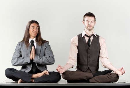Two businessmen meditating on their office deskの写真素材