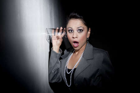 Pretty young woman using glass against wall to eavesdrop