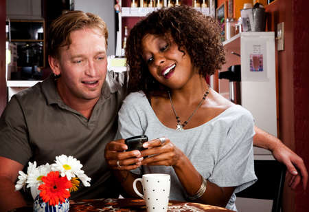 Caucasian man and African American woman in coffee house with cell phoneの写真素材