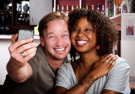 Caucasian man and African American woman taking picture in coffee house with cell phoneの写真素材